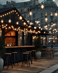Nastrojowy, zewnętrzny bar z drewnianym blatem i wysokimi stołkami, oświetlony sznurem ciepłych żarówek. W tle widoczna miejska architektura i klimatyczna wieczorna sceneria.