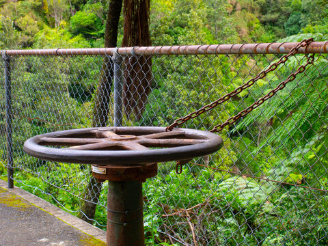 Old rusty valve wheel secured with chain by fence in forest
