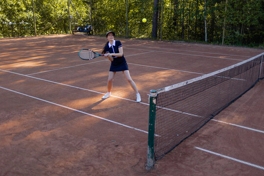 Two-handed backhand in tennis, woman meets the ball on a clay court, stroke technique.