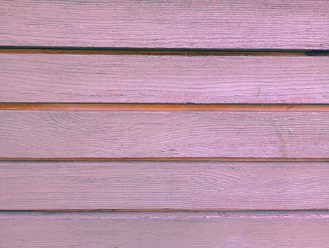 A detailed texture of horizontal wooden planks painted in a soft pastel pink mauve color, showcasing natural wood grain patterns and parallel lines for a modern rustic background.