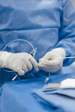 Close up of surgeon gloved hands holding syringe connected to catheter with stopcock during cardiac catheterization in hospital operating room