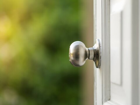 Close-up of vintage brass door knob on white wooden door with natural outdoor lighting