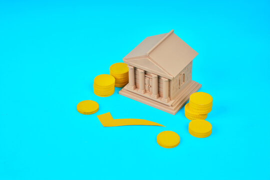 A bank building surrounded by coins and a downward arrow represents declining interest rates and reduced borrowing costs.
