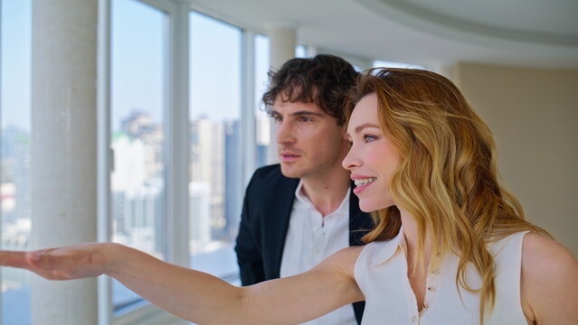 Woman pointing window showing city view luxury apartment. Couple touring flat.