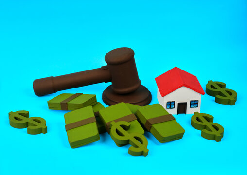 A gavel beside money bundles and a miniature house represents property auction and legal real estate transactions.
