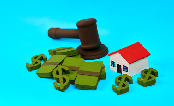 A gavel with money bundles and a miniature house represents real estate auction and property finance.
