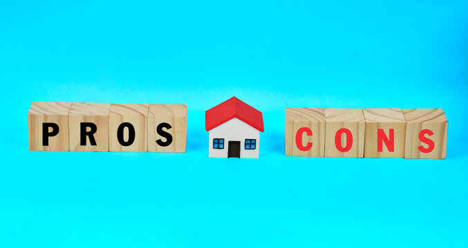 A miniature house between pros and cons blocks representing property comparison and home buying decisions.
