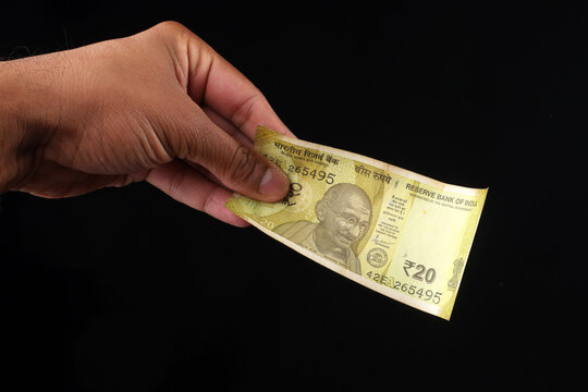 Hand holding Indian twenty rupee paper currency banknote against a dark background