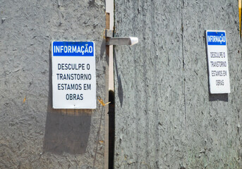 Construction site wooden hoarding with Portuguese apology and information warning signs © GezerFreitas