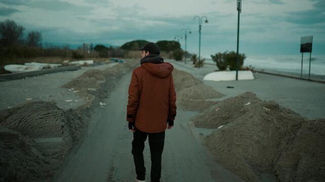 A sad man walks through the sand and destruction of a storm surge in seafront