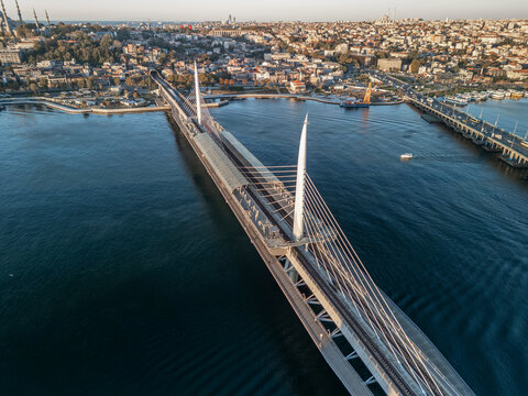 Turkey, Istanbul 06 10 2025: Sunrise drone photo with Halic Metro Bridge centered and Ataturk Bridge on right, featuring boat sailing on water and Fatih district in background.