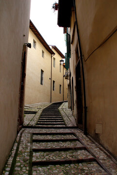 SPOLETO, ITALY - FEBRUARY 7, 2017: Streets of Spoleto. A narrow, uphill cobblestone alleyway featuring a stepped pedestrian path flanked by tall, traditional stucco buildings with windows, shutters