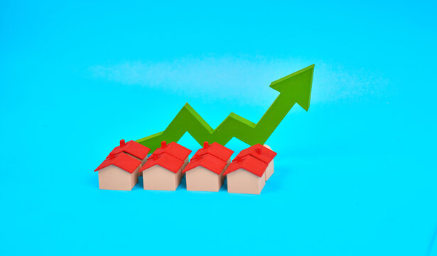 A group of miniature houses in front of an upward arrow represents increasing property values and real estate growth.
