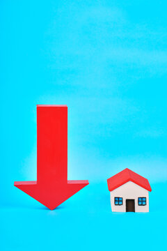 A large downward arrow beside a miniature house represents declining home values and falling real estate prices.
