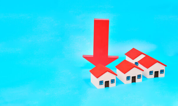 A downward arrow positioned behind miniature houses represents falling property prices and a weakening housing market.
