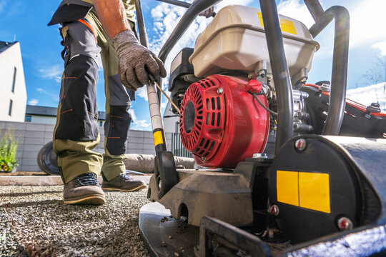 Worker starting a plate compactor on a gravel surface