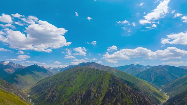 Aerial hyperlapse reveals rolling green mountains under a bright blue sky. Fluffy clouds flowing and casting shadows over grassy slopes, enhancing the natural beauty of Kyrgyzstan's wilderness.