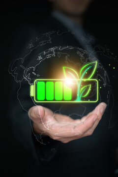 Hand holding green battery with leaves inside digital earth globe outline. Global renewable energy, sustainable power grid, environmental protection, and worldwide ESG initiatives. Vertical photo.