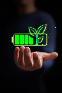 Open hand holding glowing green battery with growing small leaves, representing renewable energy, sustainable power storage, eco-friendly tech, and ESG green transition. Vertical stock photo.