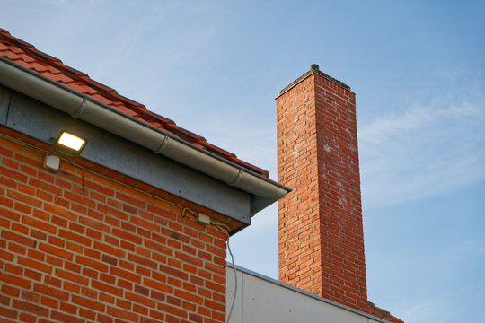 Red brick chimney and roof with gutter against clear blue sky