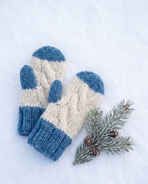 Knitted wool mittens resting on fresh snow beside a frosted evergreen branch. Cozy winter clothing concept with copy space for seasonal design and holiday greeting
