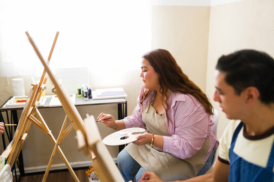 Plus size woman enjoying art class, learning to paint on canvas during a creative workshop and developing new skills