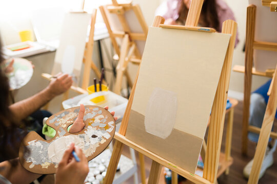 Adult student learning to paint, holding a palette with mixed colors and creating artwork on a canvas with a paintbrush