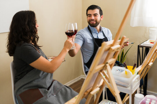 Couple enjoying a paint and sip class, toasting with red wine during a creative date night activity
