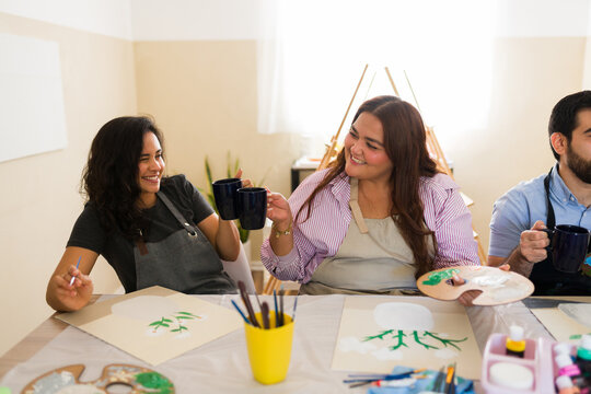 Friends enjoying art class, toasting with coffee while painting new creations and having fun together