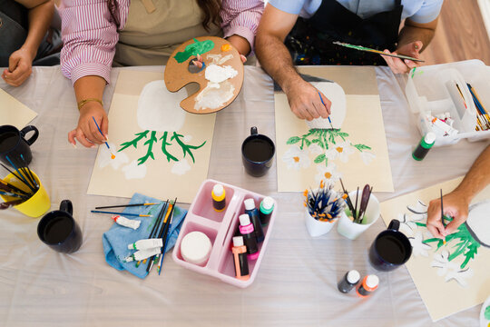 Top view of art class participants enjoying a creative painting workshop, expressing imagination on canvases with colorful paints and brushes