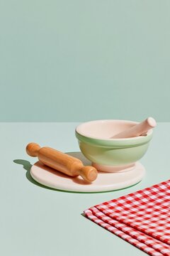 Pastel kitchen still life with ceramic mortar and pestle, wooden rolling pin and red gingham cloth on a mint green background