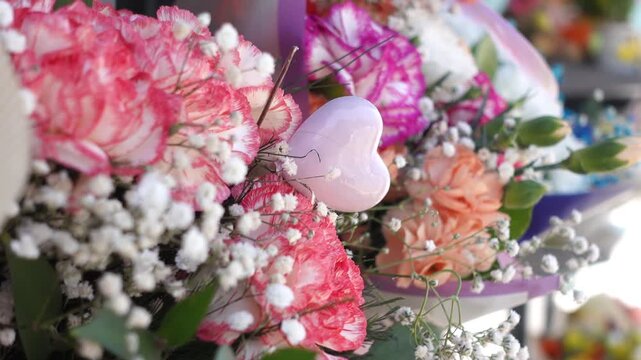 Close up of beautiful flower bouquet with pink heart ornament and carnations in florist shop