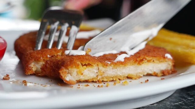 Close up video of hands cutting delicious breaded chicken cutlet with a knife and fork, served with French fries