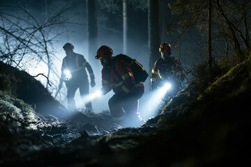 Obraz premium Firefighters navigate dark forest trails with powerful flashlights. They move cautiously through damp, mossy terrain. Their focused expressions show urgency and determination