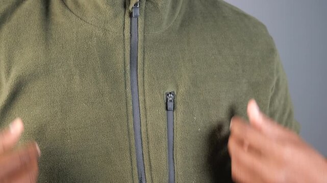 Close up shot of man zipping up green fleece jacket standing against grey background