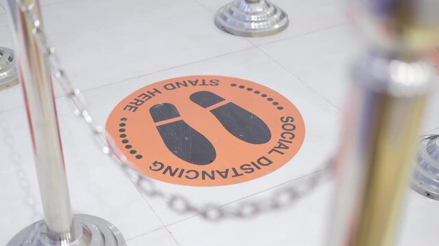 Social distancing stand here sign on floor in front of barriers during coronavirus pandemic a warning sign about social distancing