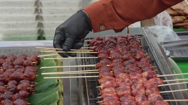 Street vendor arranging meatball skewers on a grill