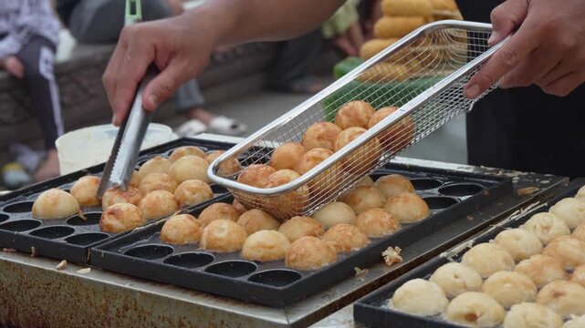Hand preparing golden round snacks on a street food griddle