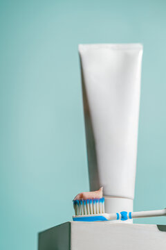 A toothbrush with blue and white bristles holds a dab of pink toothpaste in front of a dental care tube on blue background. Perfect for oral hygiene ads, dental health blogs, or product promotions.