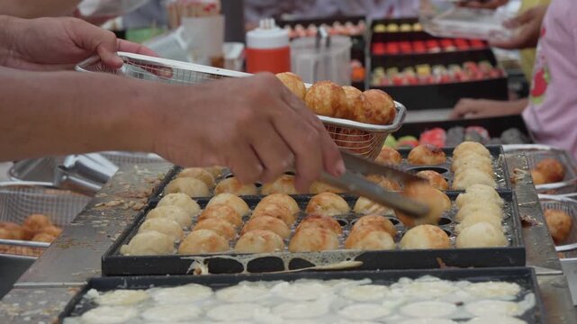Vendor preparing golden round snacks on a street food griddle