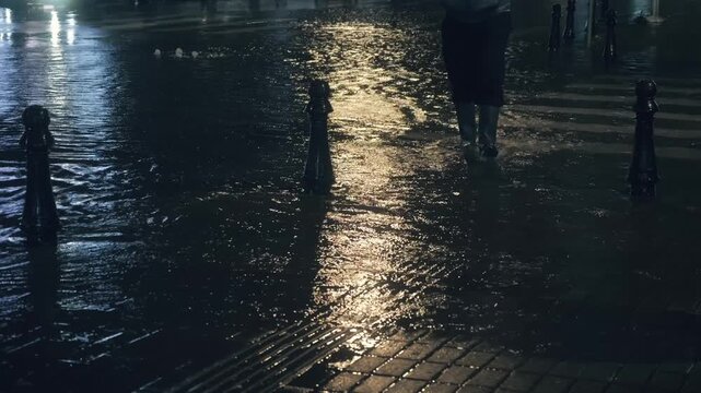 Pedestrian moving through floodwater on city crosswalk at night after intense rainfall, urban disaster scene showing dangerous street flooding, storm runoff, mobility problems and weather emergency.