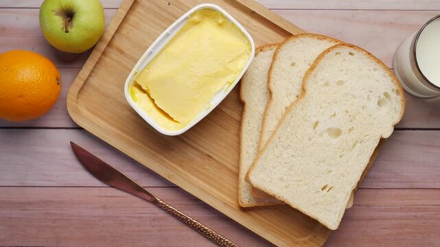 Overhead view of breakfast setting with butter, bread slices, and milk glass on wooden board