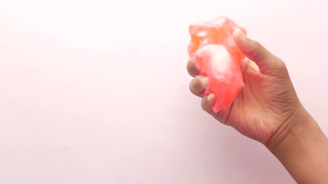 Hand squeezing bright orange translucent slime or putty on white background