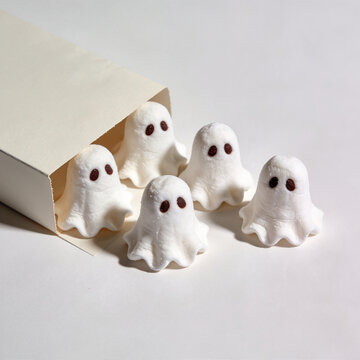 White ghost shaped meringue cookies with candy eyes on light gray surface