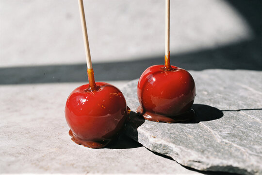 Two glossy red candy apples on wooden sticks on gray stone surface