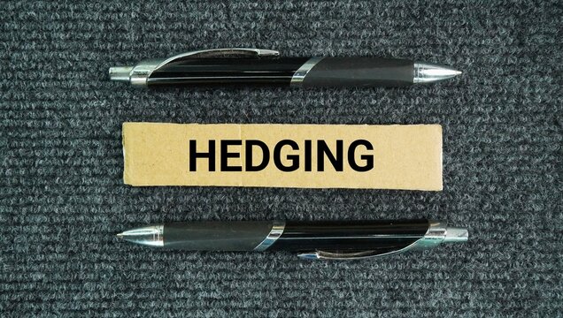 Pen and paper box with the words Hedging is a risk management strategy used to limit potential financial losses by taking an opposing position in a related asset.
