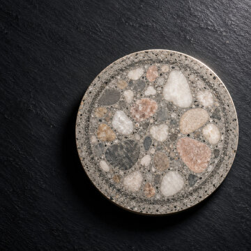 Polished low carbon concrete disc with river pebble aggregate on dark slate surface, showcasing natural stone texture and smooth finish