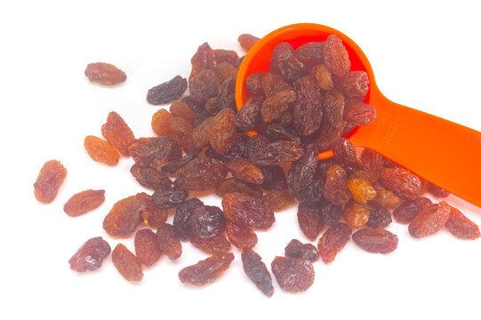 Raisins spilling out of an orange measuring spoon on white