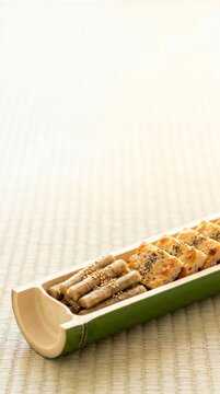 Traditional Japanese New Year appetizers tataki gobo and matsukaze chicken in green bamboo vessel vertical