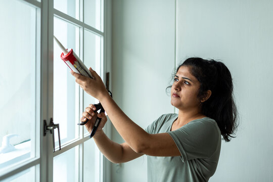 Woman sealing window with caulk